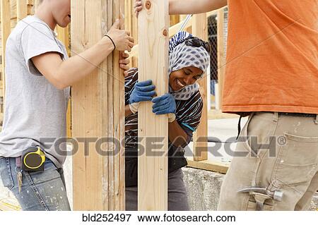 Stock Photo - Volunteers holding lumber at construction site. Fotosearch