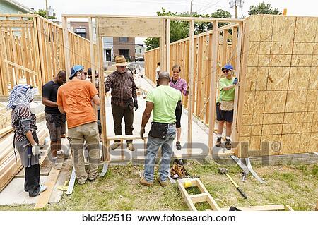 Stock Photograph - Volunteers holding wall at construction site. Fotosearch