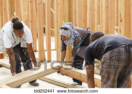 Stock Image - Volunteers lifting wooden frame at construction site. Fotosearch