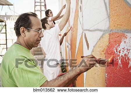 Stock Image - Volunteers painting wall together. Fotosearch