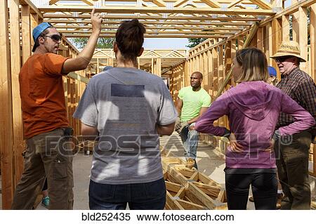 Stock Photography - Volunteers talking while building a house. Fotosearch
