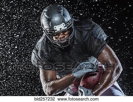 Stock Image - Water splashing on black football player. Fotosearch