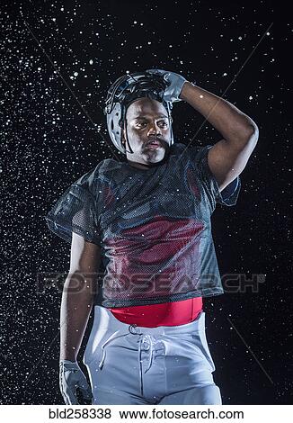Stock Photo - Water splashing on Black football player lifting helmet. Fotosearch