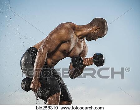 Stock Image - Water splashing on Black man lifting weights. Fotosearch