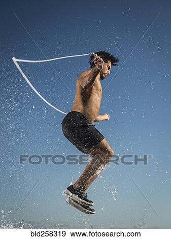 Stock Photo - Water splashing on Hispanic man jumping rope. Fotosearch