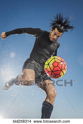 Picture - Water splashing on Hispanic man kicking soccer ball. Fotosearch