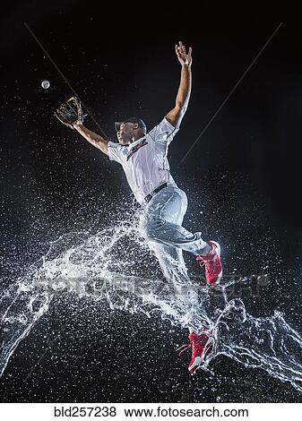 Stock Photo - Water splashing on jumping black baseball player. Fotosearch