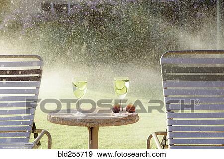 Water spraying on drinks and lounge chairs View Large Photo Image Stock Photo - Water spraying on drinks and lounge chairs. Fotosearch