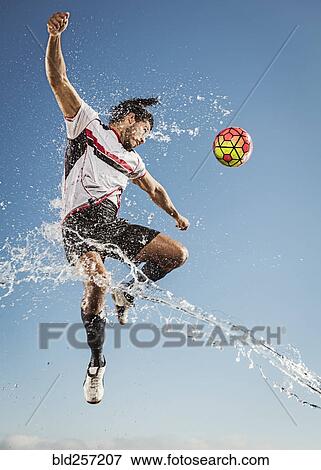 Stock Photo - Water spraying on Hispanic man heading soccer ball. Fotosearch
