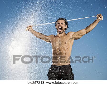 Stock Image - Water spraying on Hispanic man holding jump rope. Fotosearch