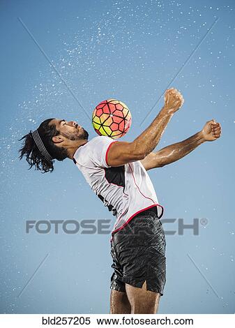 Stock Photography - Water spraying on Hispanic man trapping soccer ball on chest. Fotosearch