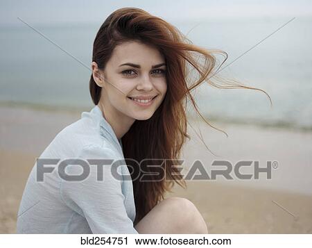 Stock Image - Wind blowing hair of Caucasian woman sitting on the beach. Fotosearch