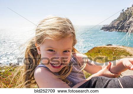 Stock Photo - Wind blowing hair of smiling Caucasian girl near ocean. Fotosearch