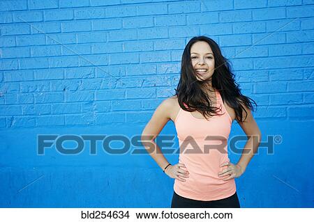 Picture - Wind blowing hair of smiling mixed race woman at blue wall. Fotosearch