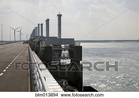 Wind turbines and dam across ocean View Large Photo Image Picture - Wind turbines and dam across ocean. Fotosearch