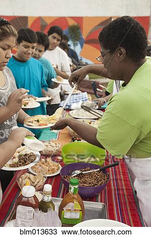 Stock Image - Woman serving people food in buffet. Fotosearch