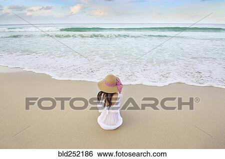 Stock Photograph - Woman sitting on beach near ocean waves. Fotosearch