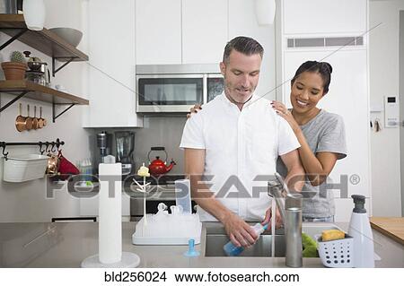 Picture - Woman watching man washing baby bottle. Fotosearch