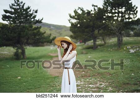 Picture - Woman wearing sun hat standing in field. Fotosearch