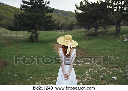 Stock Image - Woman wearing sun hat standing in field. Fotosearch
