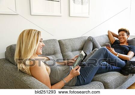 Women laying on sofa using technology View Large Photo Image Stock Image - Women laying on sofa using technology. Fotosearch