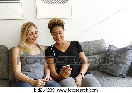Women listening to earbuds on sofa View Large Photo Image Stock Photo - Women listening to earbuds on sofa. Fotosearch