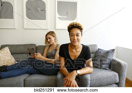 Stock Image - Women sitting on sofa using digital tablet. Fotosearch