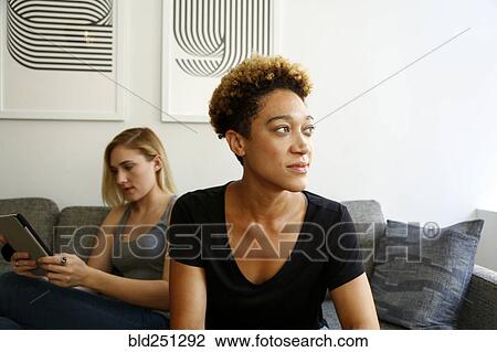 Stock Image - Women sitting on sofa using digital tablet. Fotosearch
