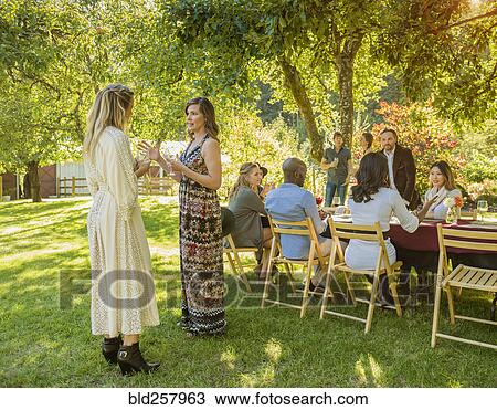 Stock Image - Women standing and talking at party outdoors. Fotosearch