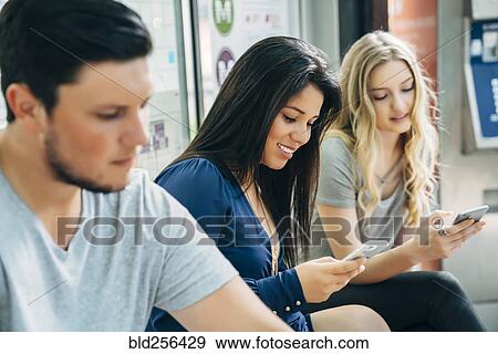 Stock Photo - Women texting on cell phones at train station. Fotosearch