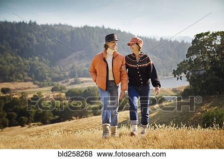 Stock Photo - Women walking arm in arm near field. Fotosearch