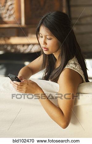 Stock Image - Asian woman text messaging on cell phone. Fotosearch