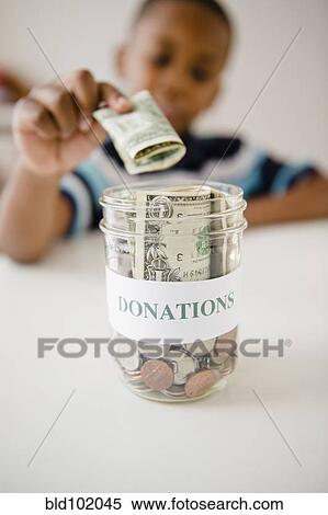 Stock Photography - Black boy putting money into donations jar. Fotosearch