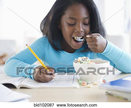 Stock Photo - Black girl eating cereal and writing in workbook. Fotosearch