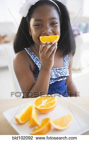 Stock Image - Black girl eating oranges. Fotosearch