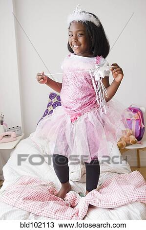 Stock Image - Black girl in fairy costume standing on bed. Fotosearch