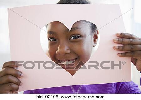 Stock Photograph - Black girl looking through heart-shaped opening in paper. Fotosearch