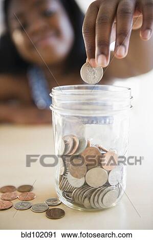 Stock Image - Black girl putting coins into a jar. Fotosearch