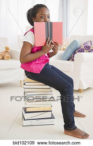 Stock Photo - Black girl sitting on stack of books reading. Fotosearch
