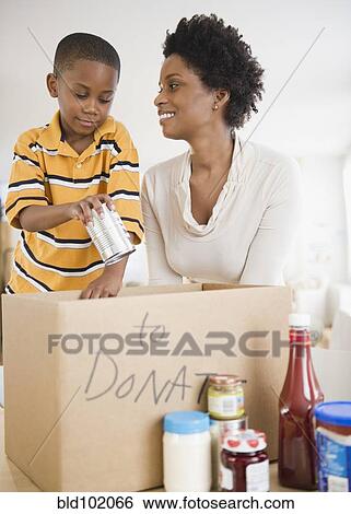 Stock Photograph - Black mother and son boxing food for donation. Fotosearch