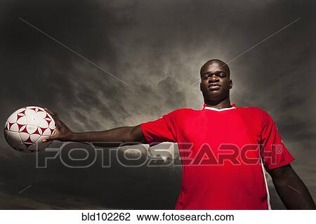 Stock Image - Black soccer player holding ball. Fotosearch