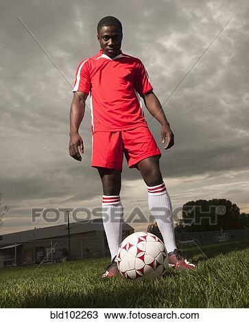 Stock Image - Black soccer player standing with ball. Fotosearch