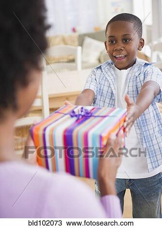 Black son handing mother a gift View Large Photo Image Stock Image - Black son handing mother a gift. Fotosearch