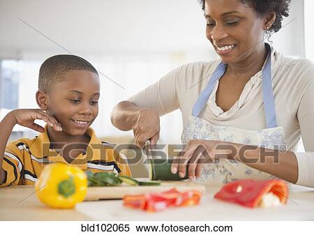 Black son watching mother slicing vegetables View Large Photo Image Stock Photography - Black son watching mother slicing vegetables. Fotosearch