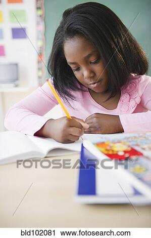 Stock Image - Black student writing in notebook in classroom. Fotosearch
