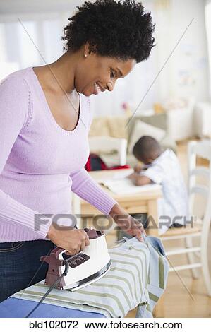 Stock Image - Black woman ironing shirt. Fotosearch