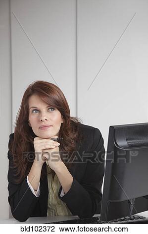 Stock Image - Businesswoman sitting at desk daydreaming. Fotosearch