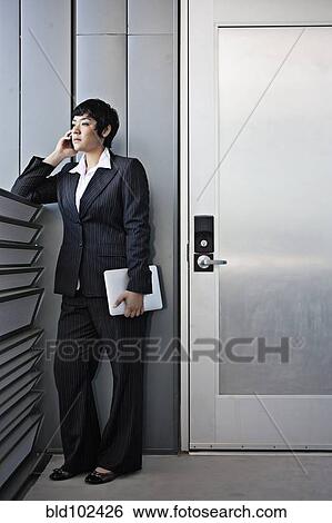 Stock Photograph - Businesswoman talking on cell phone and holding digital tablet. Fotosearch