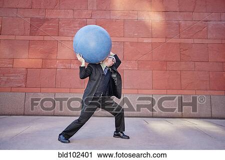 Stock Image - Caucasian businessman carrying heavy ball. Fotosearch