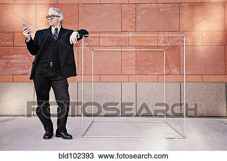 Stock Image - Caucasian businessman leaning on box and text messaging on cell phone. Fotosearch
